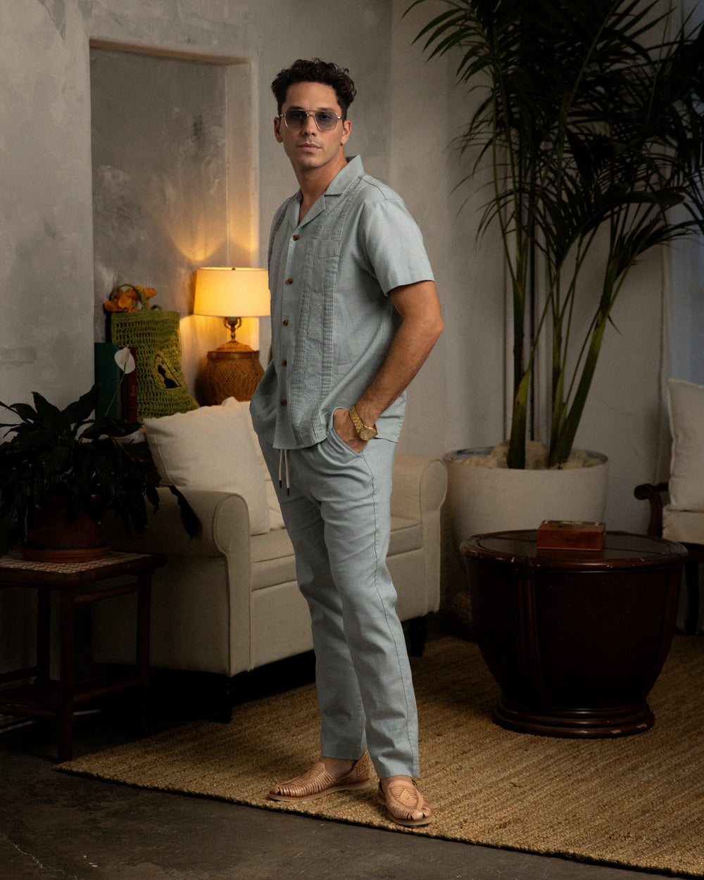 A man wearing the Dandy Del Mar Brisa Linen Pant in Abalone is standing in a living room.