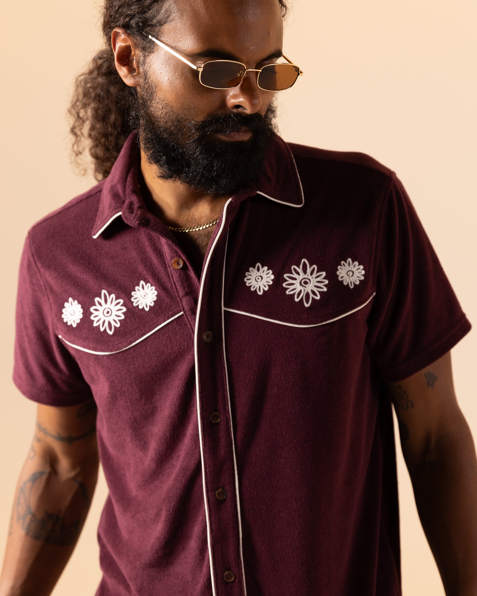 A bearded man wearing sunglasses rocks Dandy Del Mar's The Gaucho Shirt - Bordeaux, enhanced with white floral stitching, for an Equatorial Cowboy vibe.
