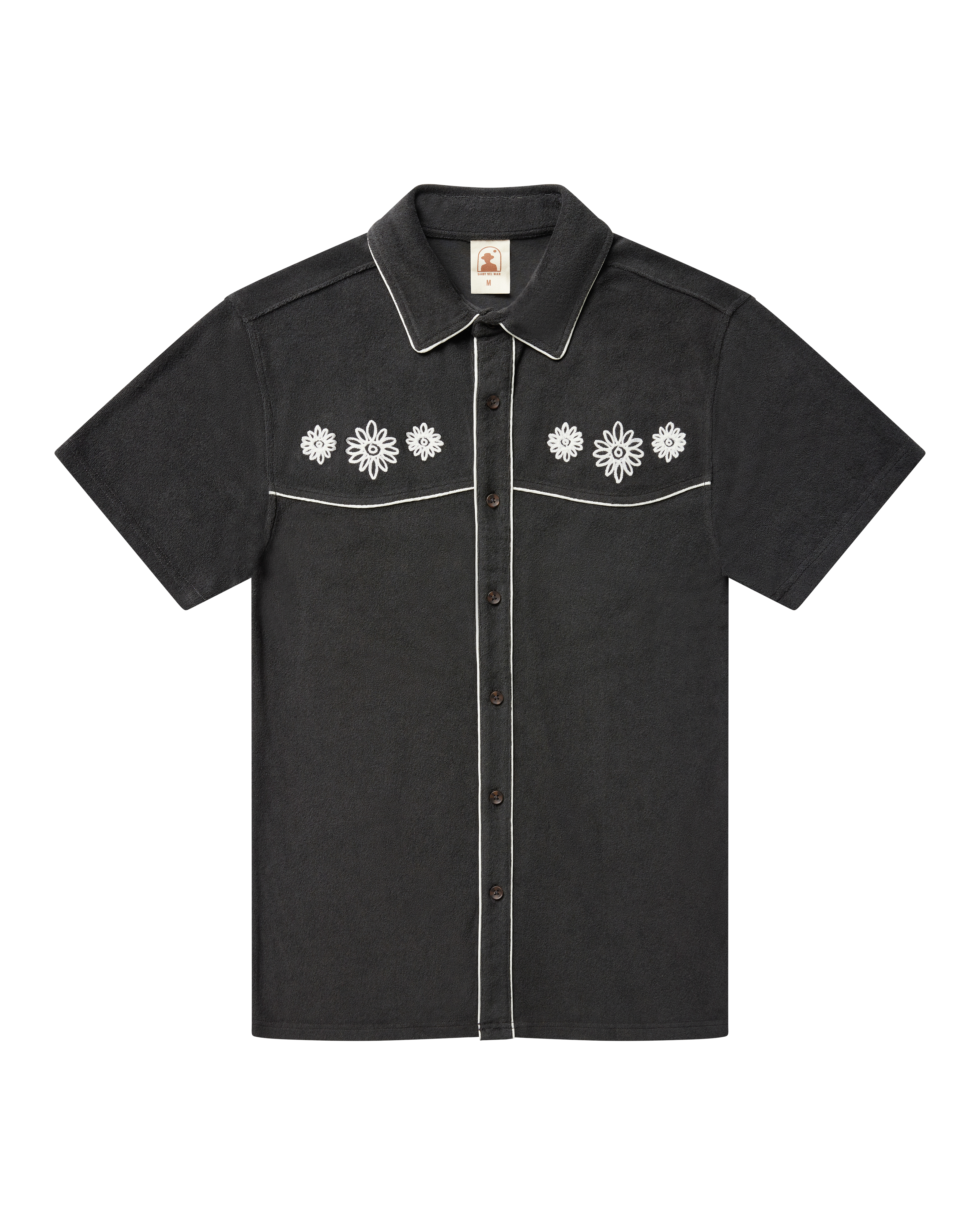 The Gaucho Shirt - Onyx by Dandy Del Mar, a short-sleeved black terry cloth shirt with white piping and embroidered floral chest, is shown laid flat on a black background.