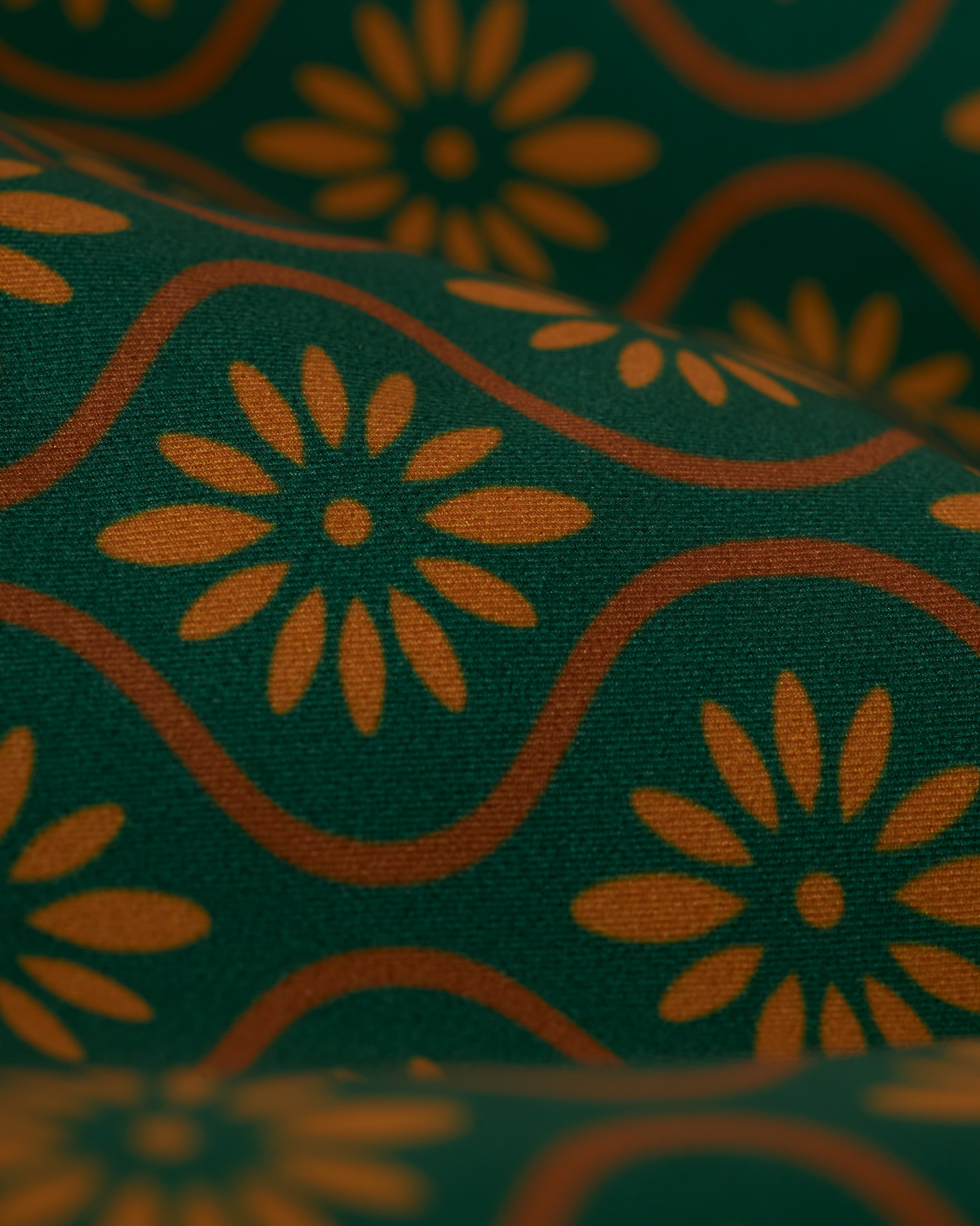 Close-up of The Cassis Square Cut Swim Brief - Albero by Dandy Del Mar, featuring a sleek European fit and a floral pattern with yellow-orange daisies and wavy lines on a dark green background, crafted from recycled polyester.