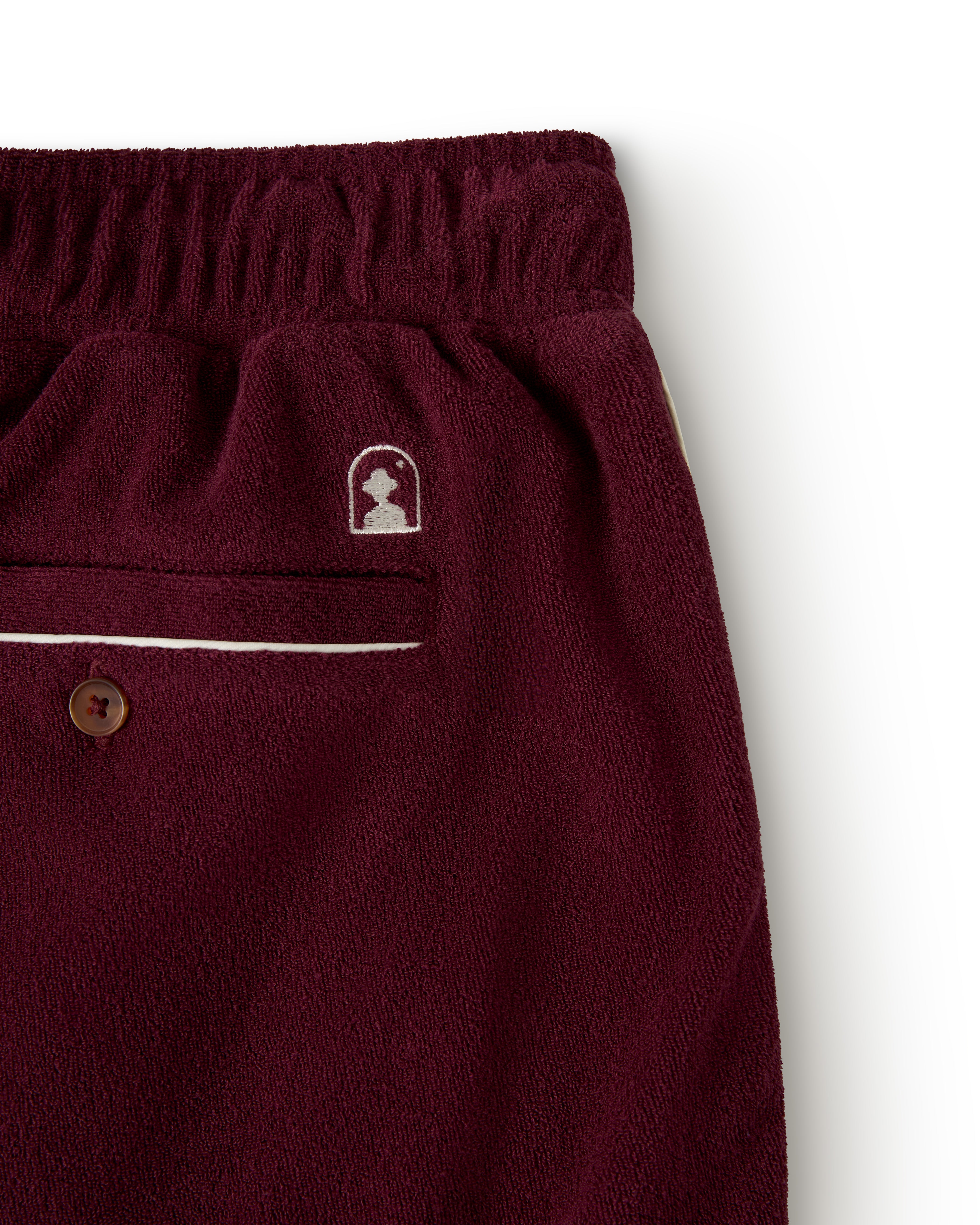 A close-up of The Gaucho Short - Bordeaux by Dandy Del Mar shows burgundy fleece pants with an elastic waistband, a single back pocket with button closure, and a small logo above it, capturing the relaxed style.