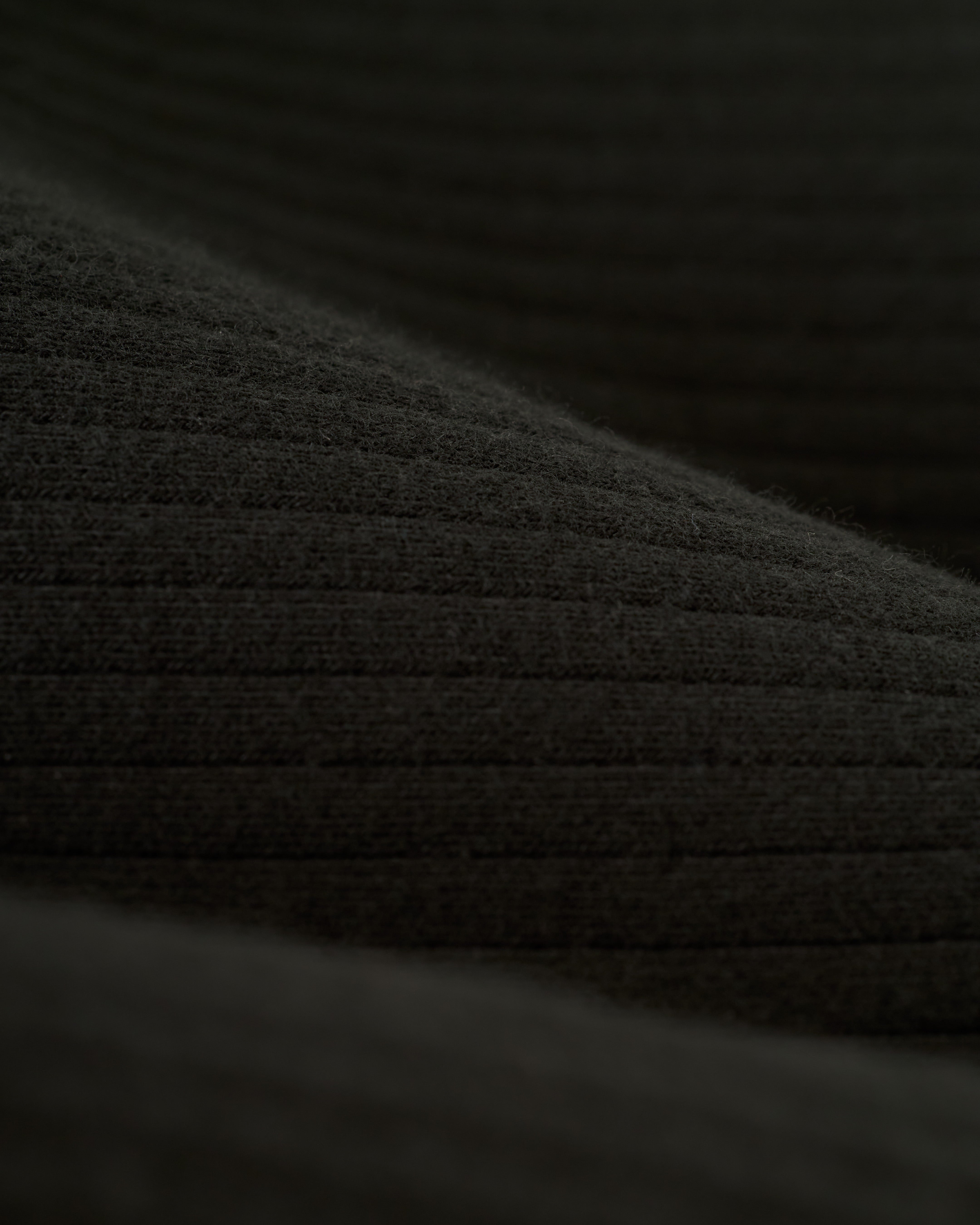 Close-up of The Milan Rib Tank - Onyx by Dandy Del Mar, featuring dark green ribbed fabric with parallel lines and a soft texture.