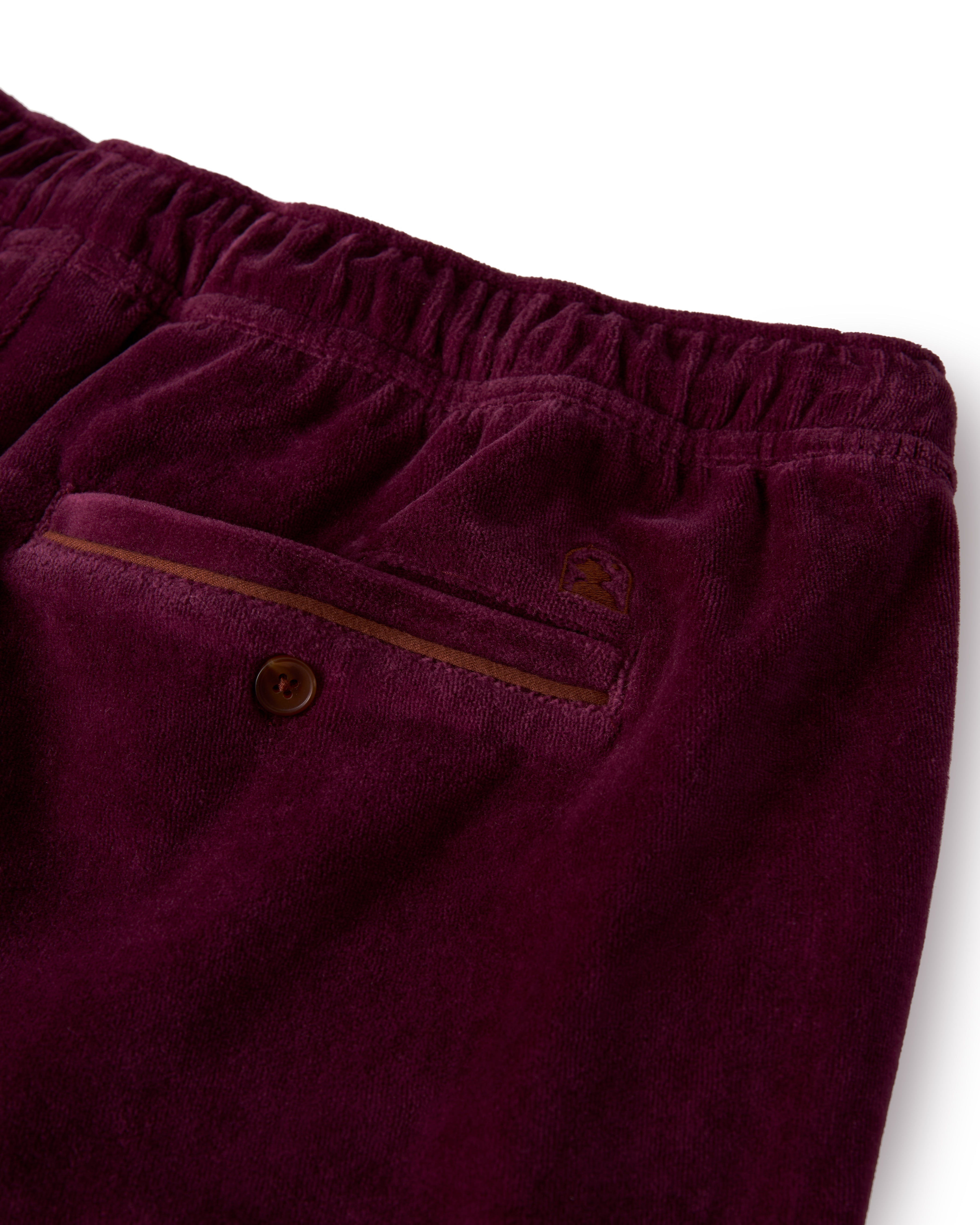 Close-up of the back pocket on The Rio Velour Short in Bordeaux by Dandy Del Mar, featuring an elastic waistband, athletic leisurewear style, button closure, and brown trim detail.