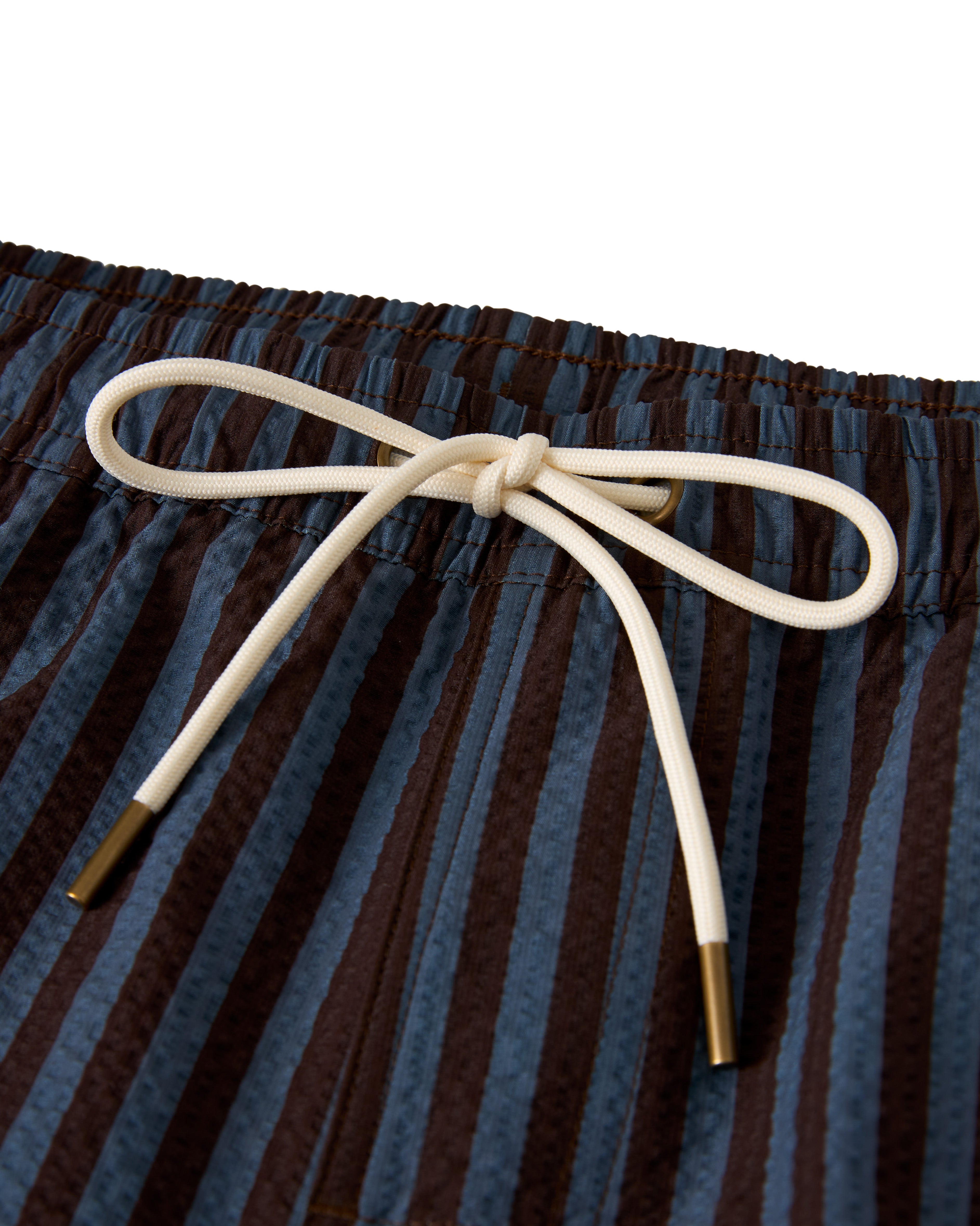 The Ventura Volley Short - Moontide by Dandy Del Mar: close-up of blue and brown striped swim shorts with an elastic waistband, a white drawstring bow, and a comfortable micro mesh liner.