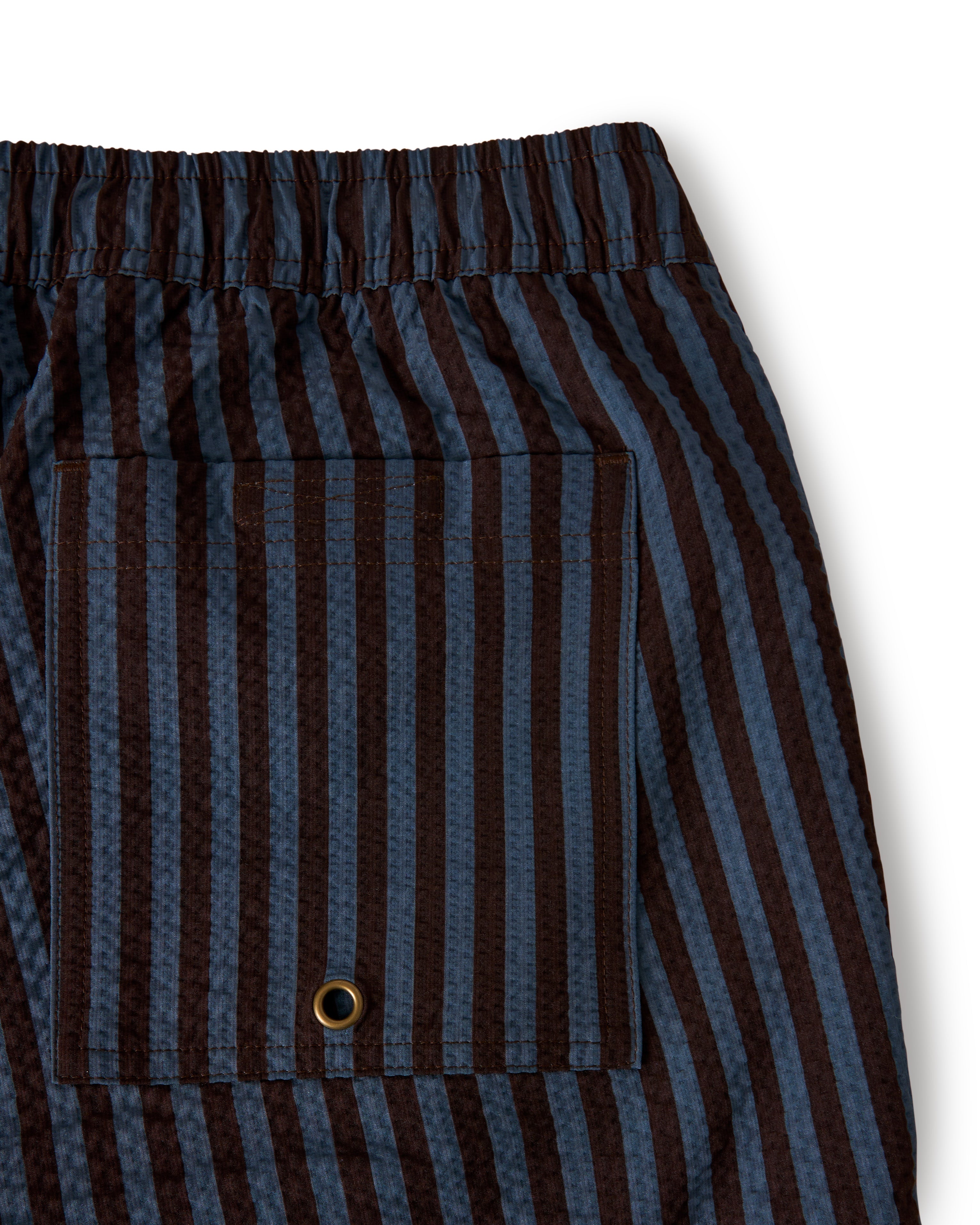 Close-up of brown and blue striped pants with an elastic waistband, resembling Dandy Del Mar's The Ventura Volley Short - Moontide, featuring a pocket with a metal eyelet.