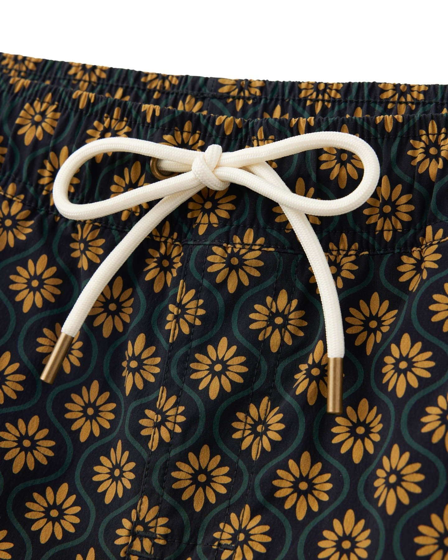 Close-up of a drawstring tied in a bow on the elastic waist of The Ventura Volley Shorts in Oro Gardenia Print by Dandy Del Mar, showcasing stylish men's swimwear with yellow and green floral patterns.