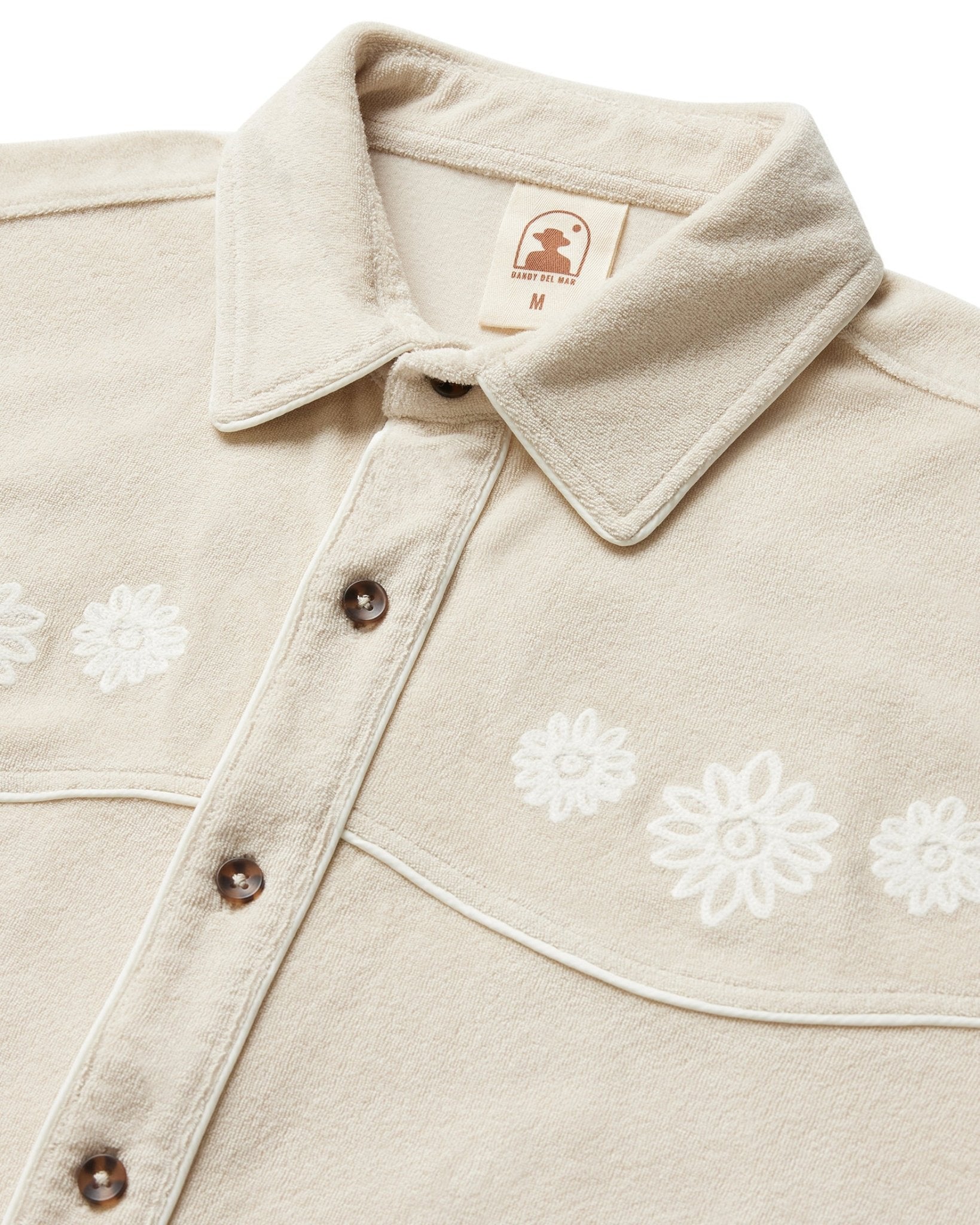 The Dandy Del Mar Gaucho Terry Cloth Shirt in Alabaster features white floral embroidery and a pointed collar, shown from the chest up.