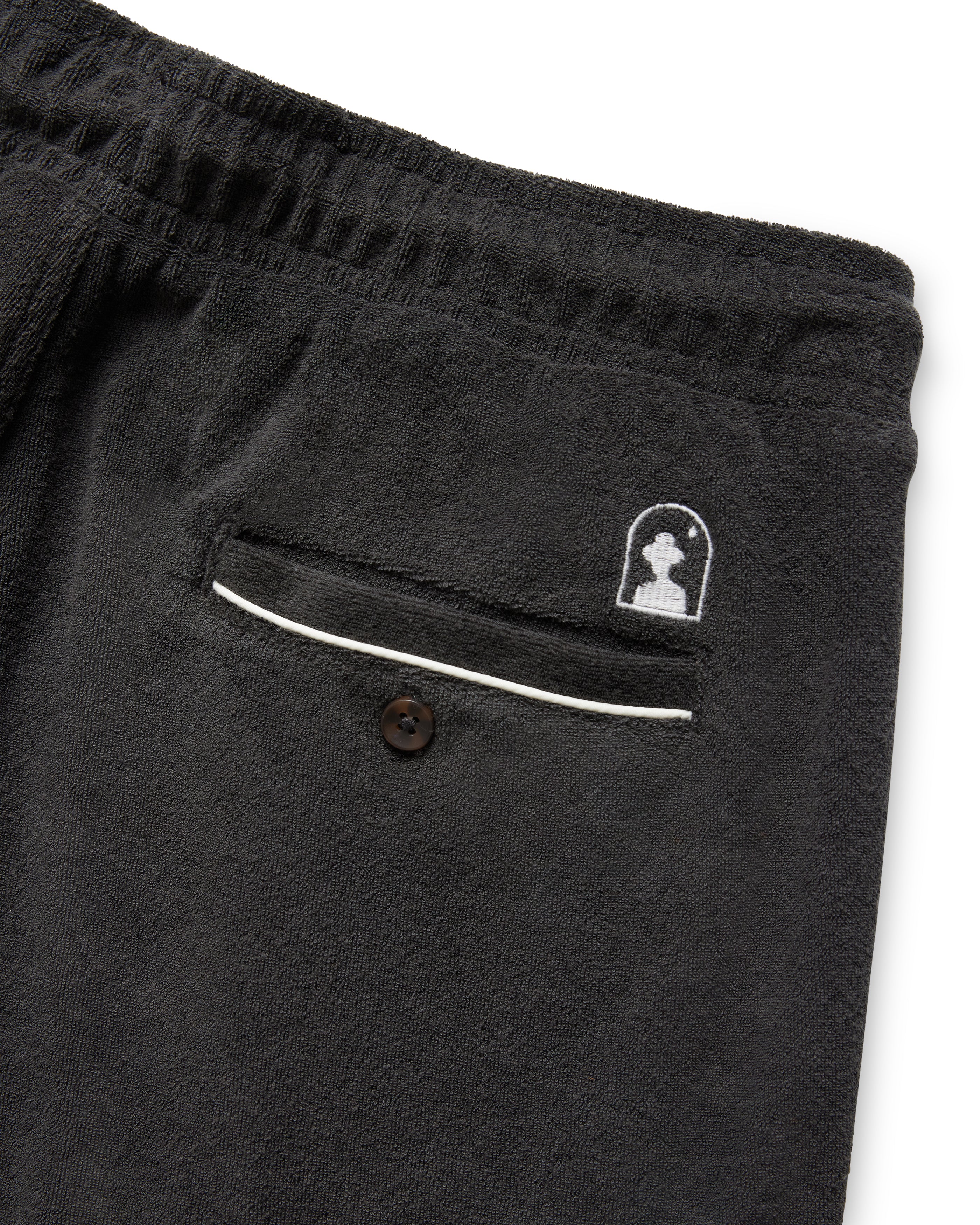 Close-up of Dandy Del Mar's The Gaucho Shorts - Onyx, showcasing a back pocket with button, white piping, and a small embroidered silhouette logo.