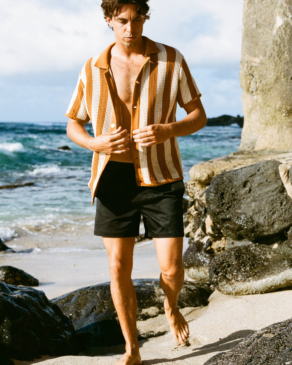 man on rocky beach in Dandy Del Mar's black short and orange & white shirt  
