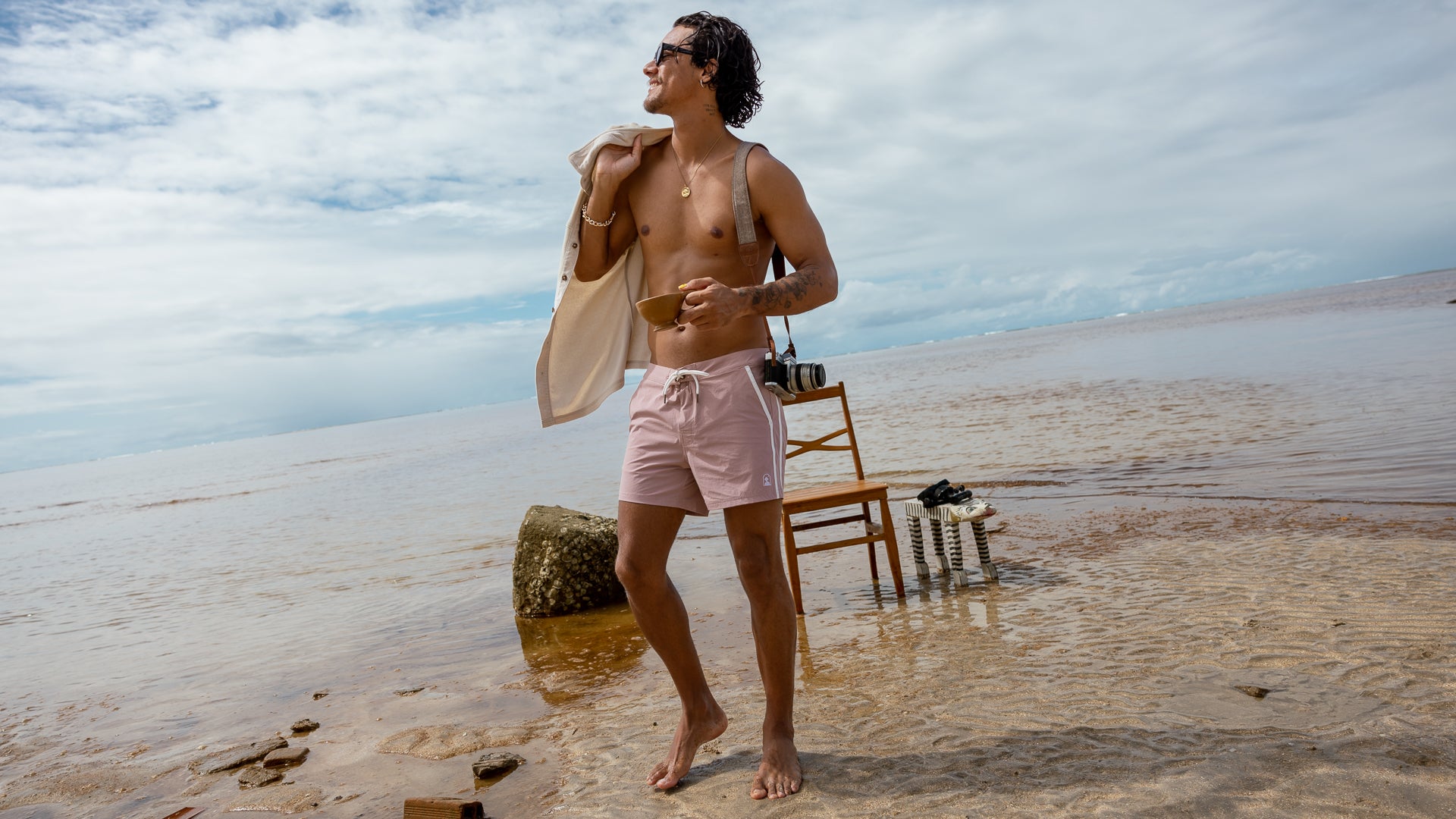 man in swim shorts on beach with camera