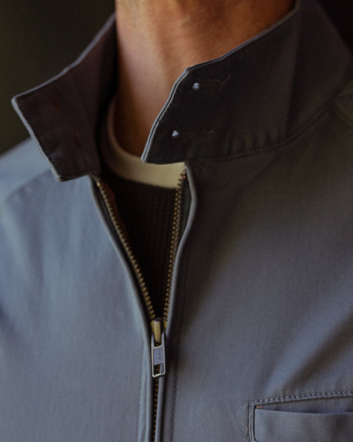 Close-up of a person wearing a gray, lightweight Rhodes Jacket - Abyss by Dandy Del Mar with a zipped-up collar.