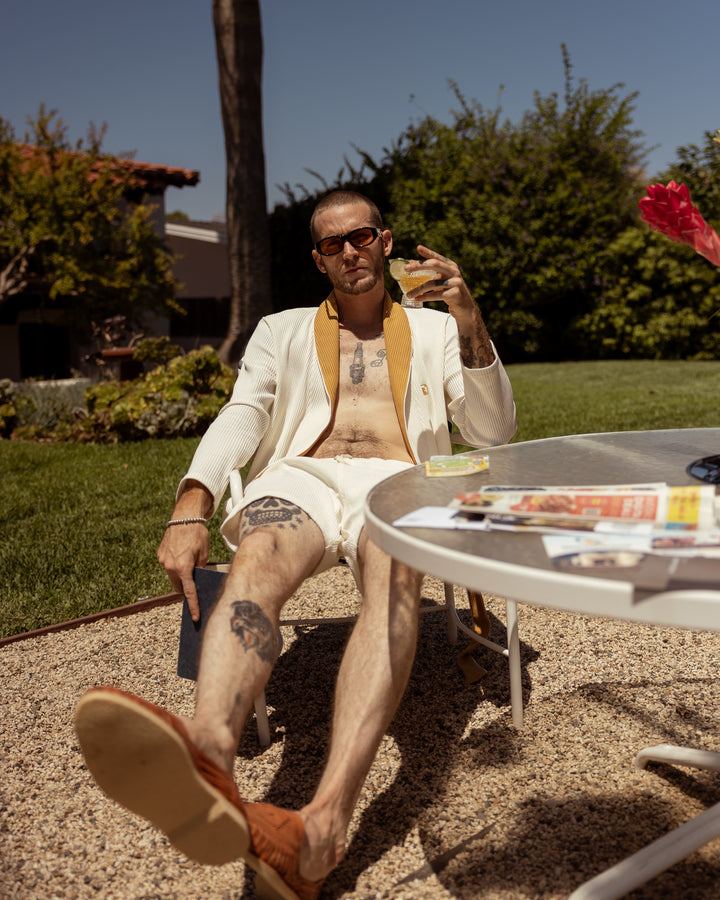 A man sitting in a lawn chair with The Cannes Waffle Knit Robe - Vintage Ivory by Dandy Del Mar.