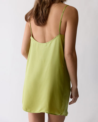 A person with long brown hair is shown from the back wearing Dandy Del Mar's The Adonia Satin Slip Dress in Lime, featuring thin straps, against a plain background.