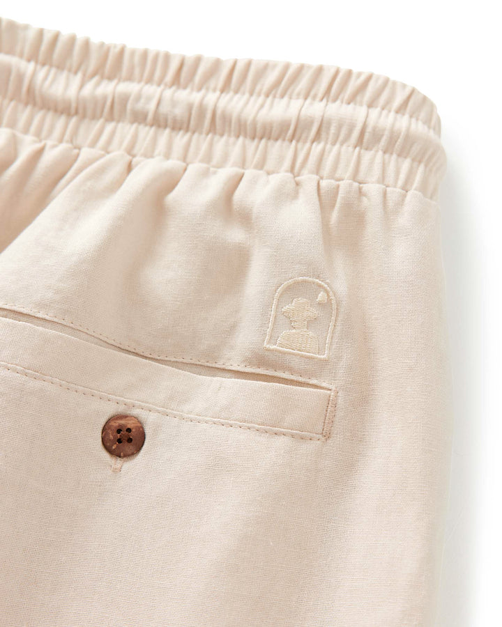 A pair of The Brisa Linen Pant - Vintage Ivory by Dandy Del Mar with a button on the side.