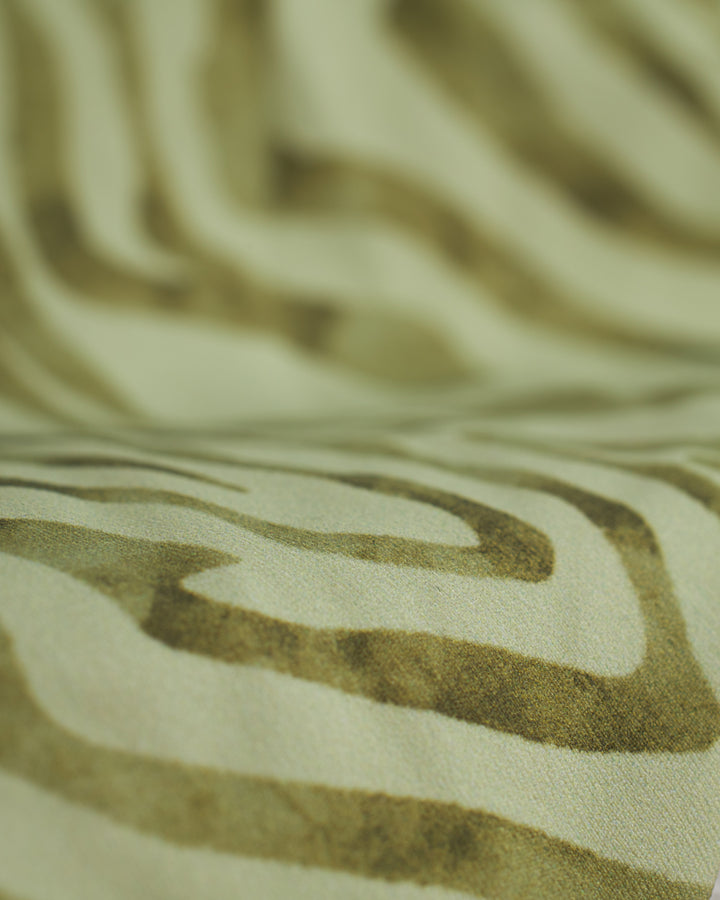 Close-up of beige fabric with irregular brown wave-like patterns, reminiscent of The Gomera Bottom - Arbequina by Dandy Del Mar.