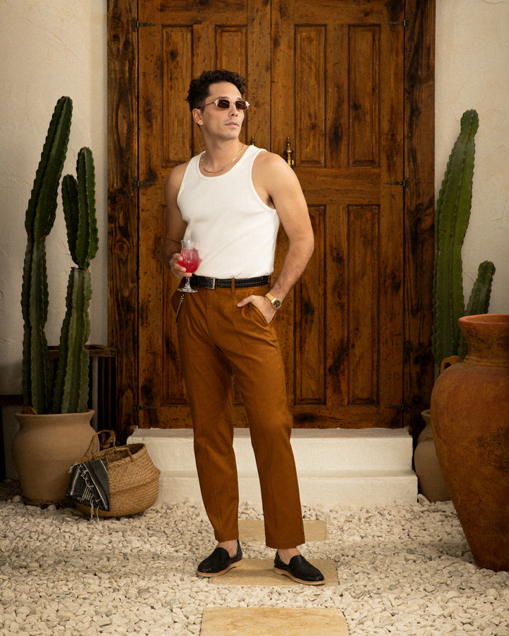 A man in a white tank top and tan pants standing in front of a cactus, dressed in a Dandy Del Mar Brisa Linen Trouser - Sedona.