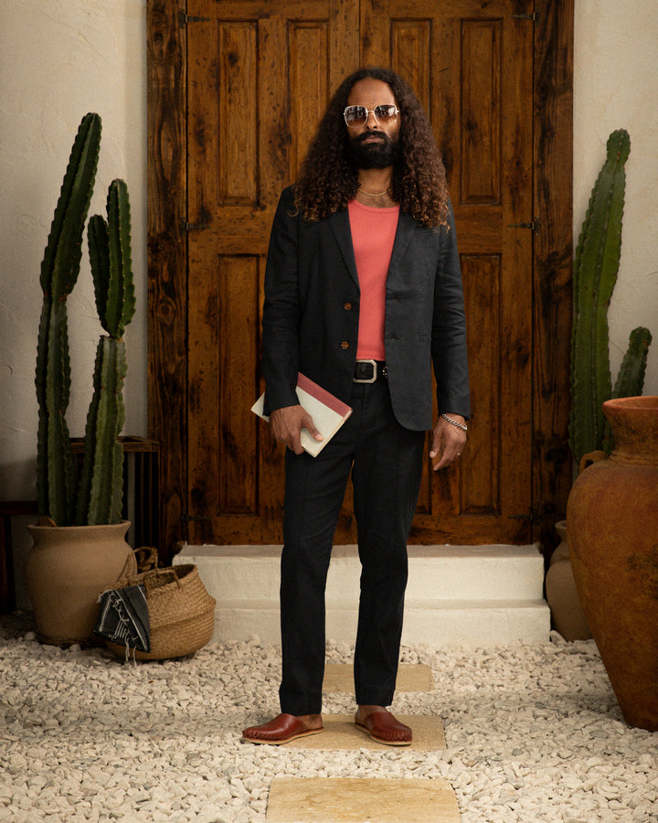 A man wearing a Dandy Del Mar Brisa Linen Blazer - Onyx stands in front of a door adorned with cacti.