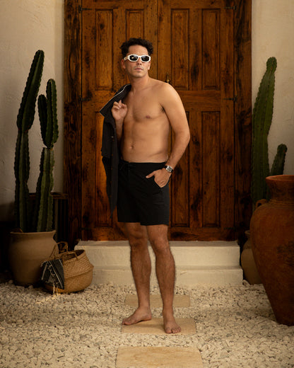 A man in Dandy Del Mar's Cavoli Swim Short - Onyx, made with performance fabric featuring 4-way stretch, standing in front of a cactus.