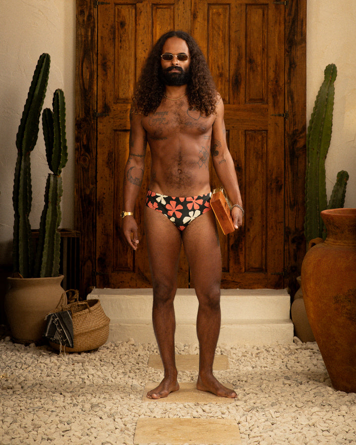 A man in The Belize Swim Brief - Currant by Dandy Del Mar standing next to a cactus.