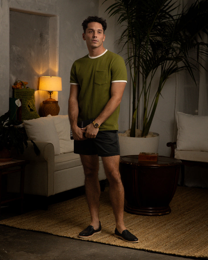 A man standing in a living room wearing a contrast collar Dandy Del Mar Arbequina Cannes Tee.