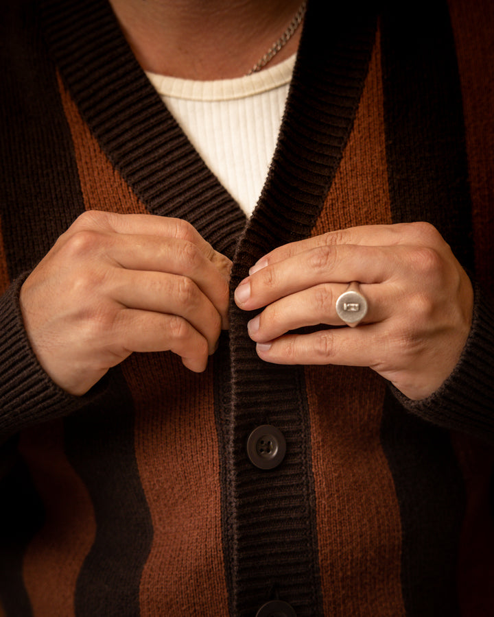 A person buttoning The Florence Knit Cardigan - Garam by Dandy Del Mar, featuring a brown and black jacquard knit, wears a silver ring on the left hand.