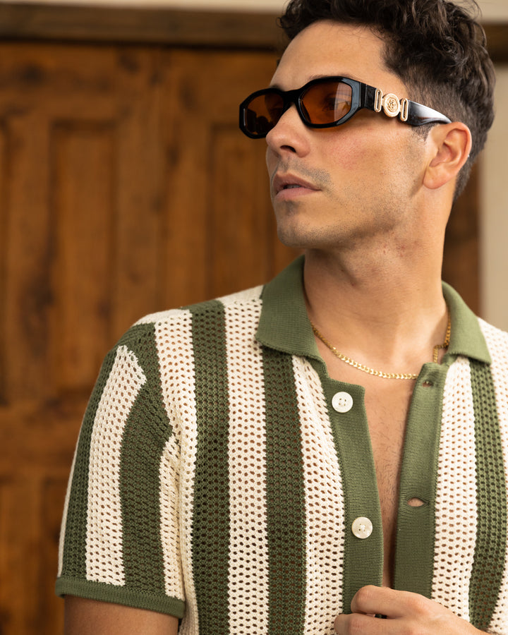 A man donning a cotton crochet Arbequina Crochet Shirt from Dandy Del Mar with sienna stripes, completing his look with sunglasses.