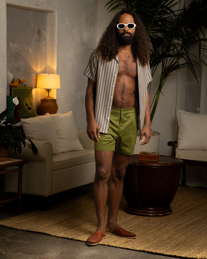 A man wearing The Mallorca Short - Arbequina by Dandy Del Mar, with adjustable antique brass side fasteners, standing in a living room.