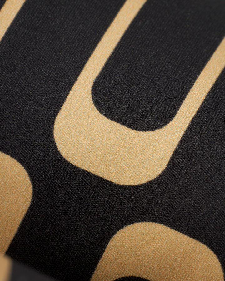 Close-up view of a Dandy Del Mar The Gomera Top - Albatross fabric with large gold letters on a black background. The texture of the recycled nylon and the sharp edges of the letters are clearly visible.