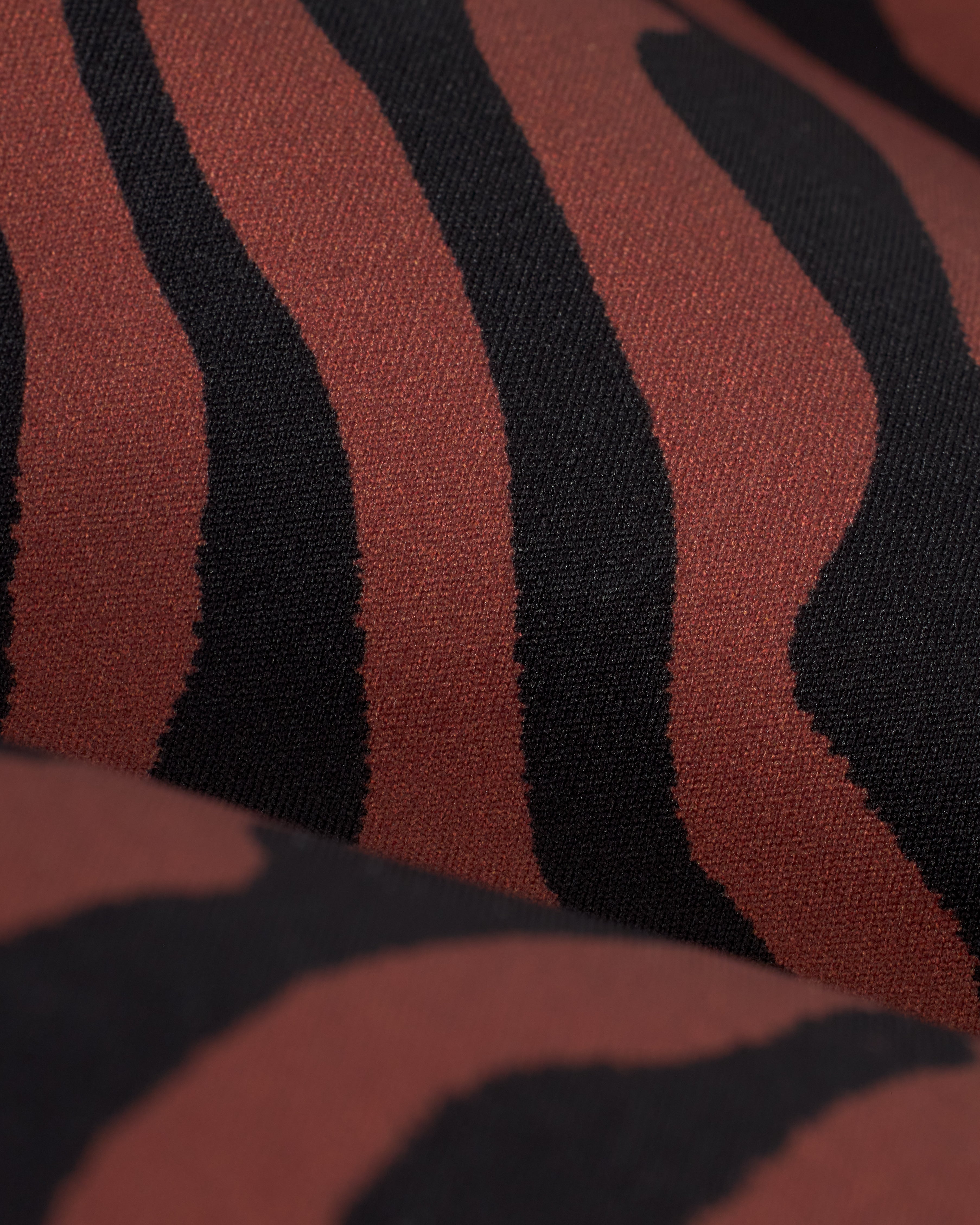 Close-up of The Hierro Top - Onyx fabric by Dandy Del Mar, featuring a minimalist pattern of wavy black stripes on a brown background.