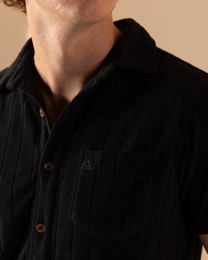 Wearing Dandy Del Mar's The Tropez Jacquard Shirt in Onyx, with its short sleeves, wooden buttons, left-side pocket, and a small emblem, captures the relaxed elegance of the Côte d'Azur.