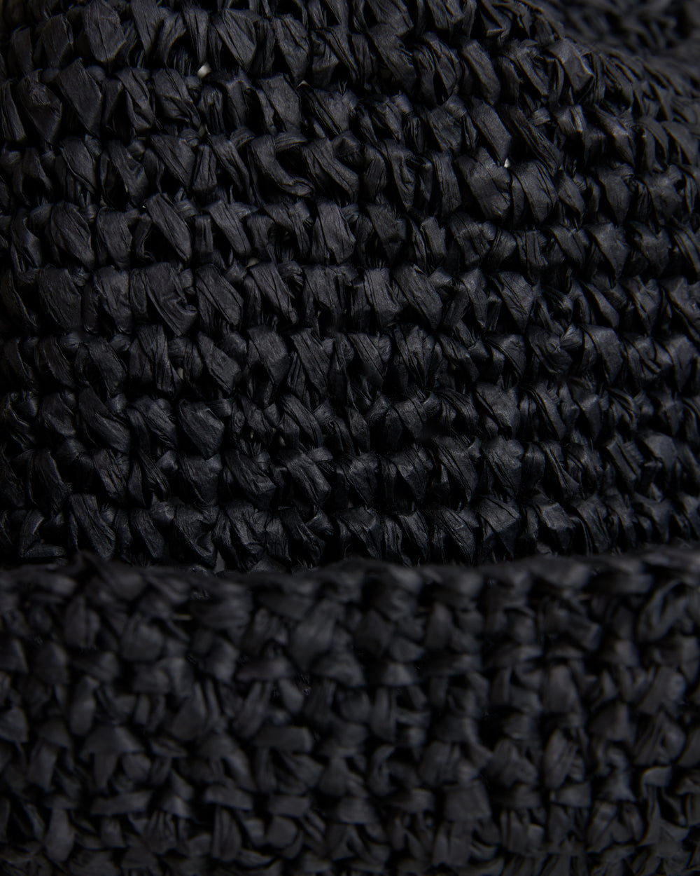 Close-up of The Amabile Rafia Hat - Onyx from Dandy Del Mar, a textured black fabric with a detailed woven pattern, highlighting the intricate threads and fibers.