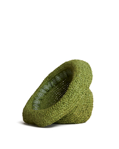 A product image of The Amabile Raffia Hat - Verde by Dandy Del Mar, showcasing a green hat with a slightly tilted, hypertrophic design and an intricate white pattern along the inner rim, featuring a raffia-effect crochet texture, placed on a plain white background.