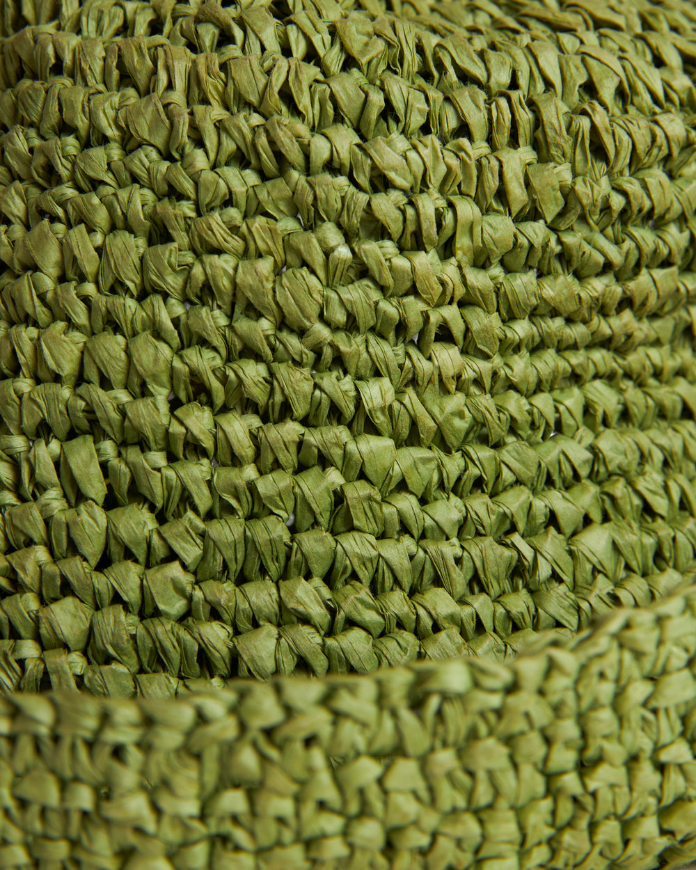Close-up view of a textured surface made from closely woven green fibers, exhibiting a detailed and dense pattern of The Amabile Rafia Hat by Dandy Del Mar.