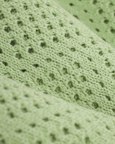 Close-up of the Dandy Del Mar Antibes Crochet Polo Shirt in Pistachio, featuring a light green knit with a repeating pattern of small holes.