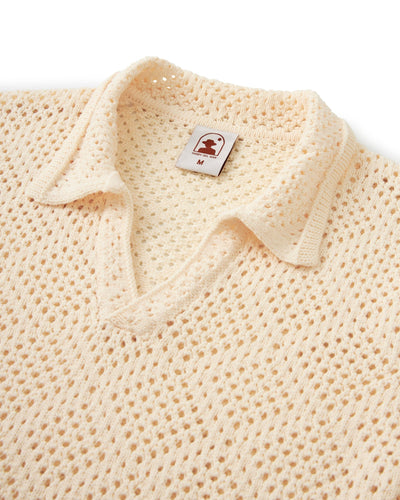 Close-up of The Antibes Crochet Polo Shirt by Dandy Del Mar in Vintage Ivory, featuring a diamond pattern, V-neck, open-knit collar, and size M tag.