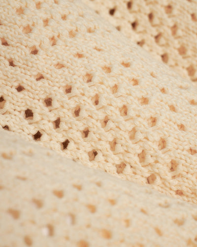 Close-up of The Antibes Crochet Polo Shirt in Vintage Ivory by Dandy Del Mar, showcasing its beige cotton material with a repeating openwork pattern and textured stitches for a crochet-inspired look.