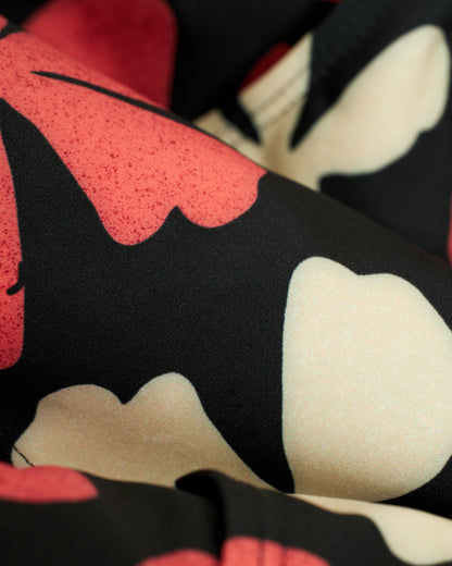 Close-up of Dandy Del Mar's The Belize Swim Briefs - Currant, featuring a bold black, red, and cream floral pattern in recycled polyester. Soft-looking with abstract leaf shapes, it's ideal for those embracing an epicurean lifestyle.