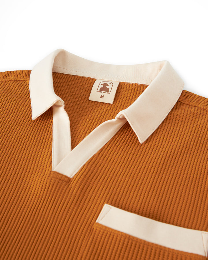 Close-up of a rust-colored waffle-knit **Dandy Del Mar The Cannes Waffle Knit Shirt - Burnt Sienna** with a beige polo collar, V-neckline, and a small pocket, labeled as size M.