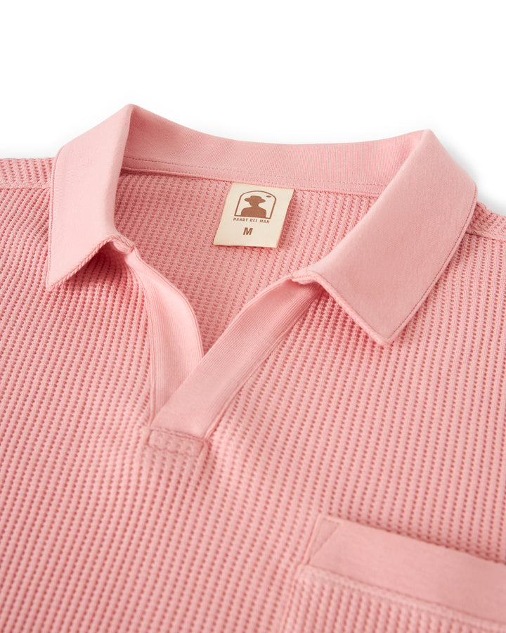 Close-up of a buttonless polo-collar pink shirt made of waffle-knit fabric, featuring a front pocket and a size M label inside the collar. Product Name: The Cannes Waffle Knit Shirt - Spanish Rose by Brand Name: Dandy Del Mar