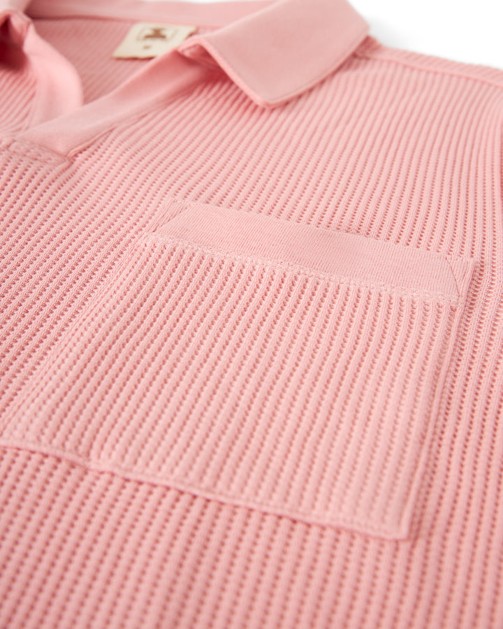 Close-up of a pink textured short-sleeve The Cannes Waffle Knit Shirt - Spanish Rose by Dandy Del Mar with a front pocket. The collar and placket feature a smoother fabric compared to the waffle knit texture of the rest of the shirt.