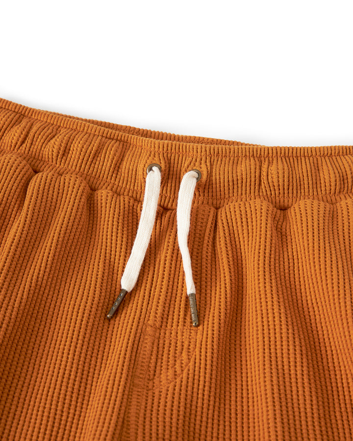 Close-up of The Cannes Waffle Knit Shorts - Burnt Sienna by Dandy Del Mar, with a white drawstring at the elastic waistband, made from waffle knit fabric.