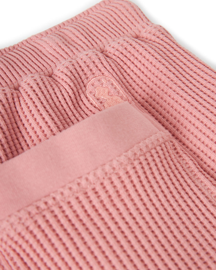 Close-up of The Cannes Waffle Knit Shorts - Spanish Rose by Dandy Del Mar, showcasing a pink, textured, waffle knit fabric with ribbed patterns, featuring a stitched emblem and a smooth band.