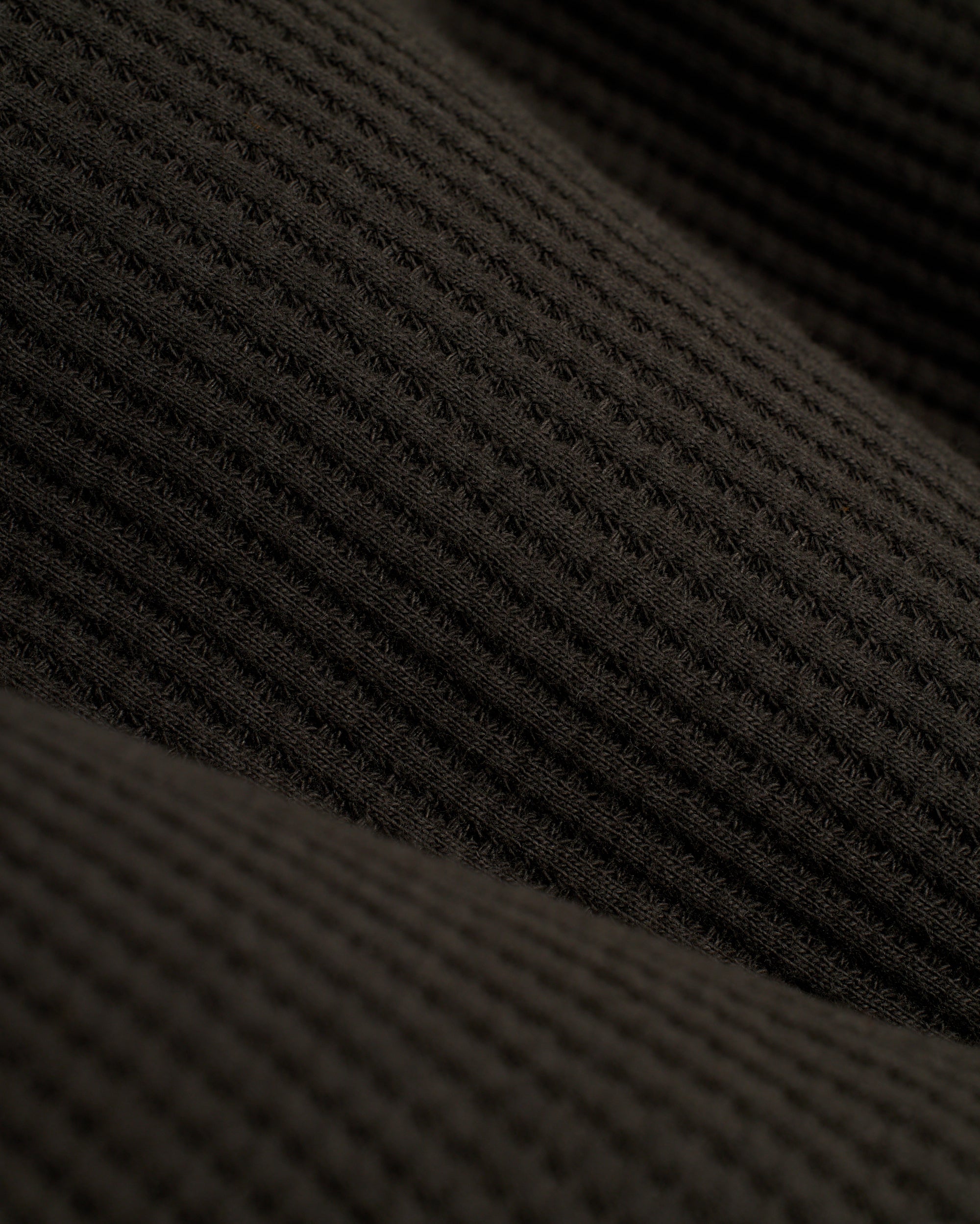 Close-up of dark gray, waffle knit textile with horizontal ridges and dimples from Dandy Del Mar's The Cannes Waffle Knit Tee - Albatross, known for its breathable fabric.