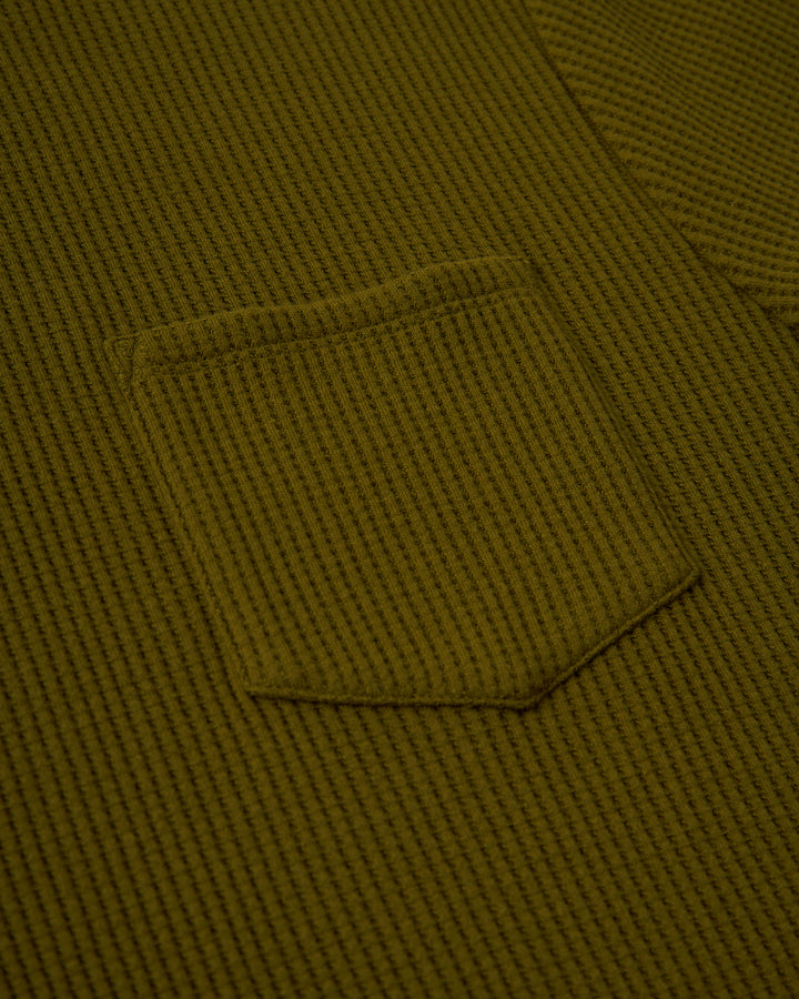 A close up of a green Cannes Tee - Arbequina from Dandy Del Mar with a pocket.