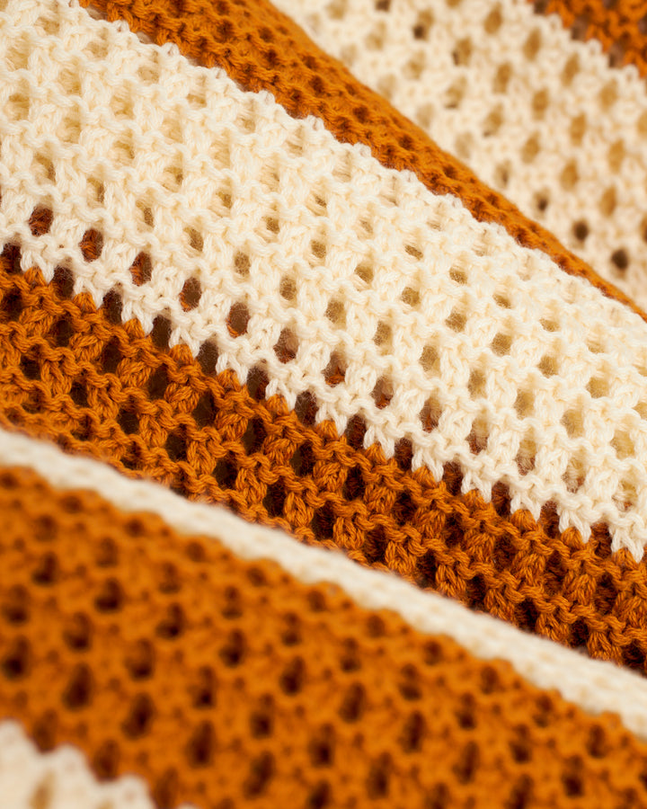A close up of The Dominica Crochet Shirt - Burnt Sienna Stripe, a Dandy Del Mar cotton crocheted blanket.