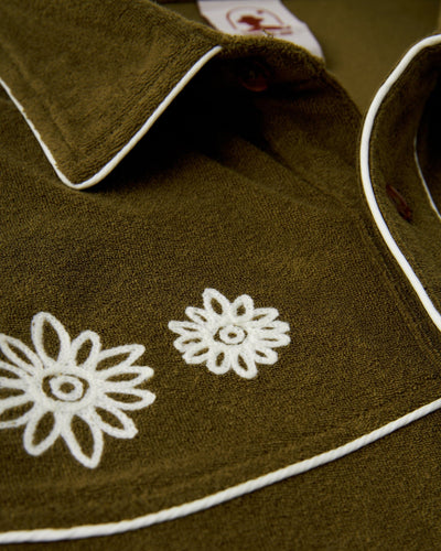 Close-up of Dandy Del Mar's The Gaucho Terry Cloth Shirt - Arbequina in olive green, featuring white floral embroidery and white piping along the collar and seams.