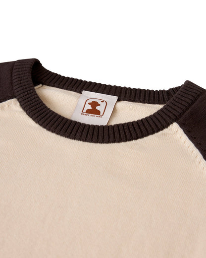 Close-up of The Grenada Sweater Knit Baseball Tee - Tierra by Dandy Del Mar—a beige and brown lightweight cotton crewneck with ribbed collar, featuring a silhouette logo and "SABOR DEL MAR" label for vintage-sport style.
