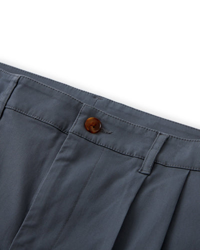 Close-up of the waistband of Dandy Del Mar's The Rhodes Twill Shorts - Abyss, featuring blue-gray washed cotton twill, a brown button, belt loops, and front pleats.