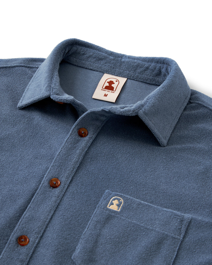 The Tropez Shirt - Annapolis for men by Dandy Del Mar features a tailored fit and is made with terry cloth fabric. This stylish shirt is designed in a timeless blue color and showcases a unique brown patch on the chest.