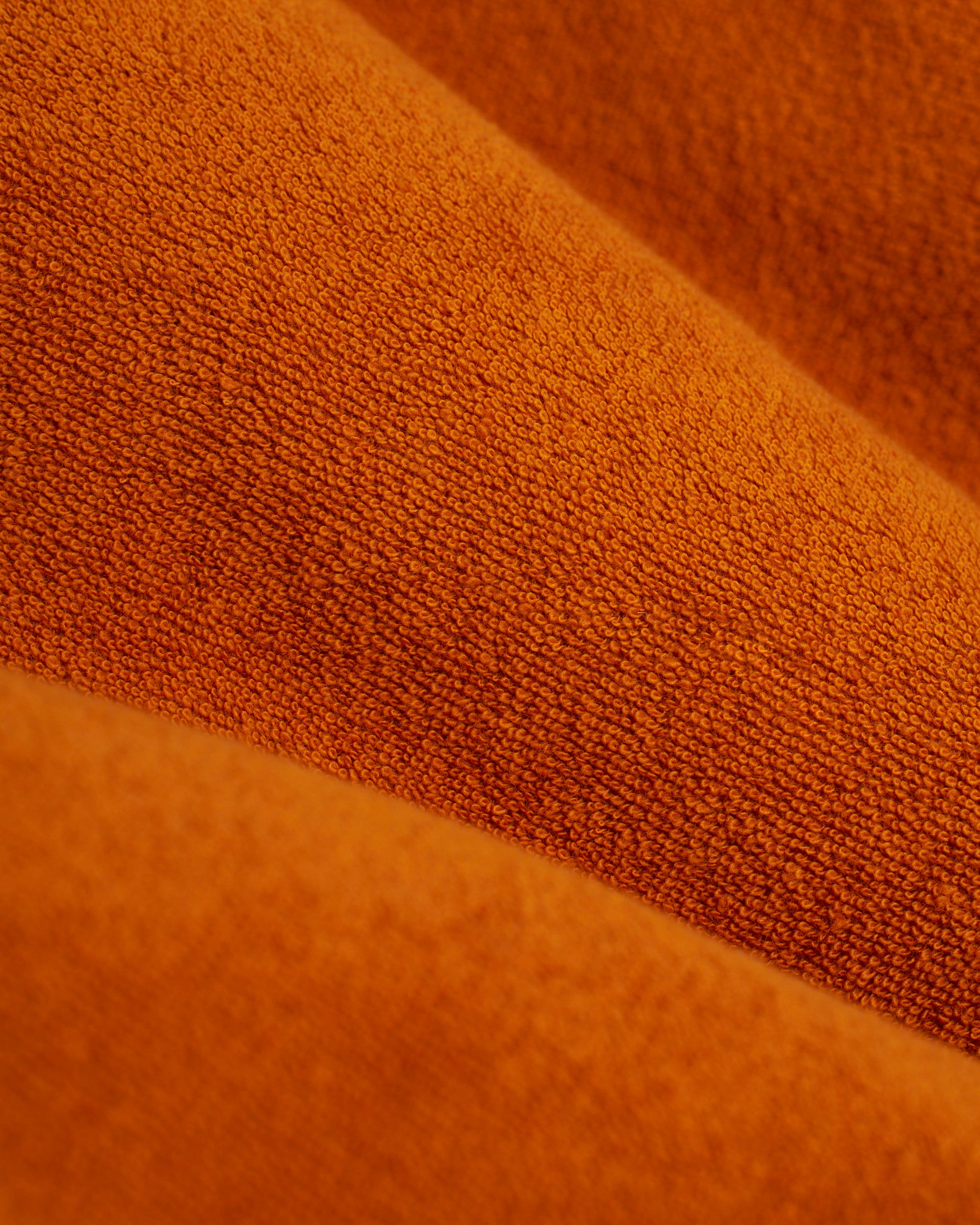 Close-up of orange terry cloth fabric with visible weave and diagonal folds, reminiscent of Dandy Del Mar’s stylish Tropez Short in Burnt Sienna seen along the Côte d'Azur.